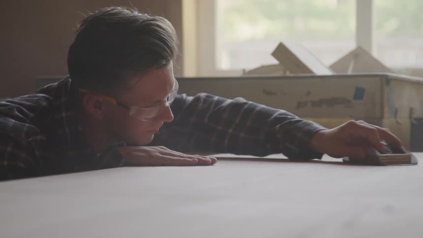 A man is low over a wooden surface as he sands it