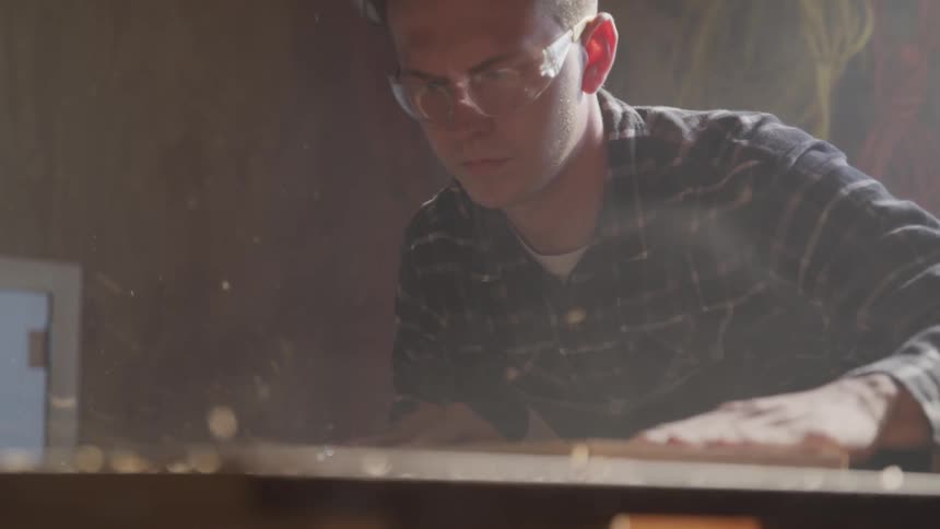 Young man works with a piece of wood in a workshop