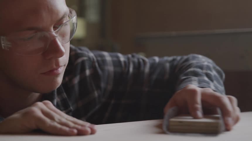 A man inside with protective goggles sanding a piece of wood
