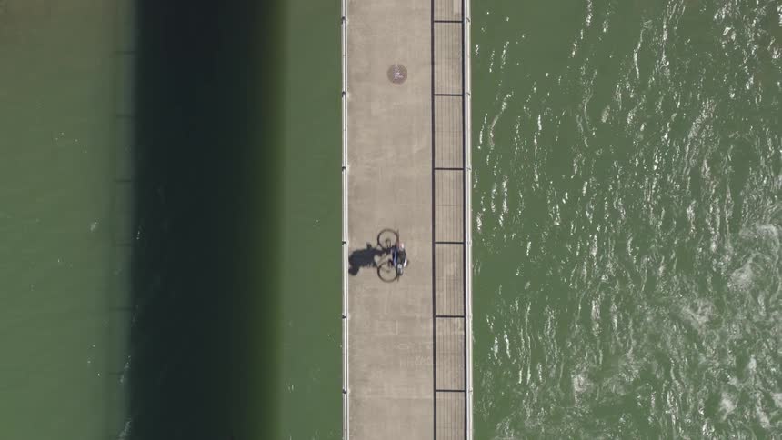 A bicyclist rides across a long narrow bridge over the water