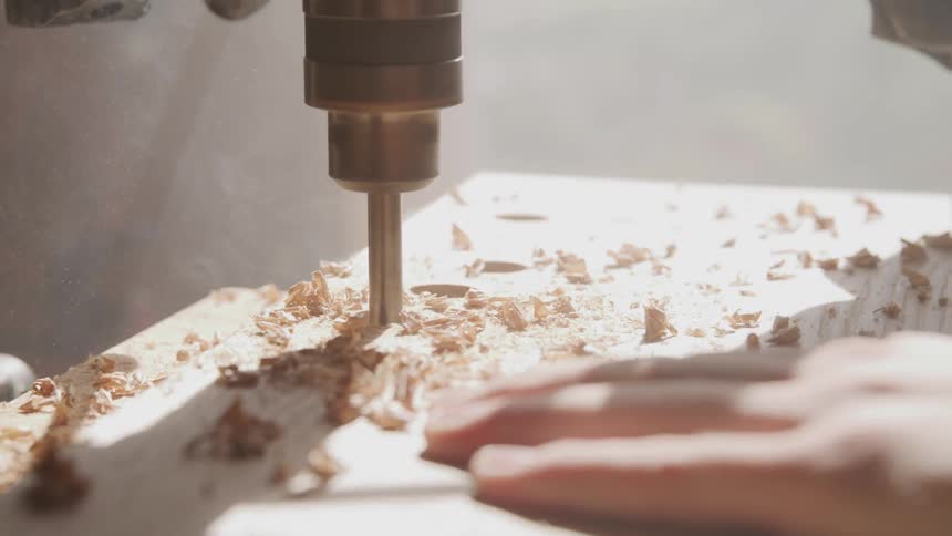 A man drilling a hole through a wood plank