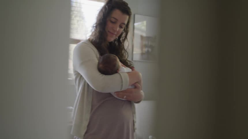 A new mom looks down at her baby as she rocks and sways while holding him