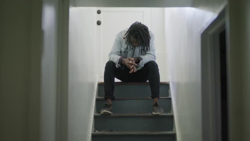 A man sits at the top of stairs indoors