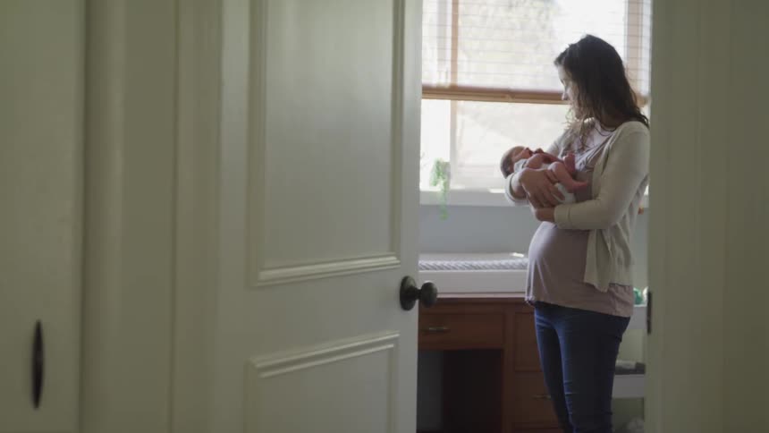 A mother is standing in a nursery holding her new born baby and talking while gently bouncing and rocking back and forth