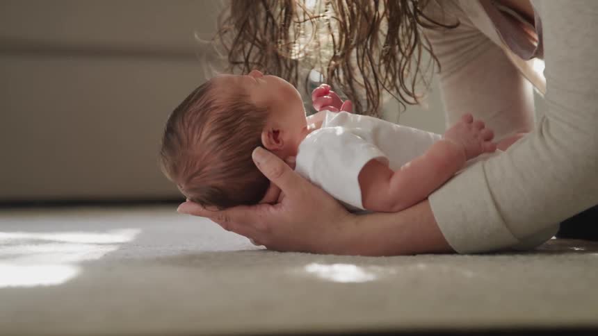 A woman holds a small baby in her arms and leans over him