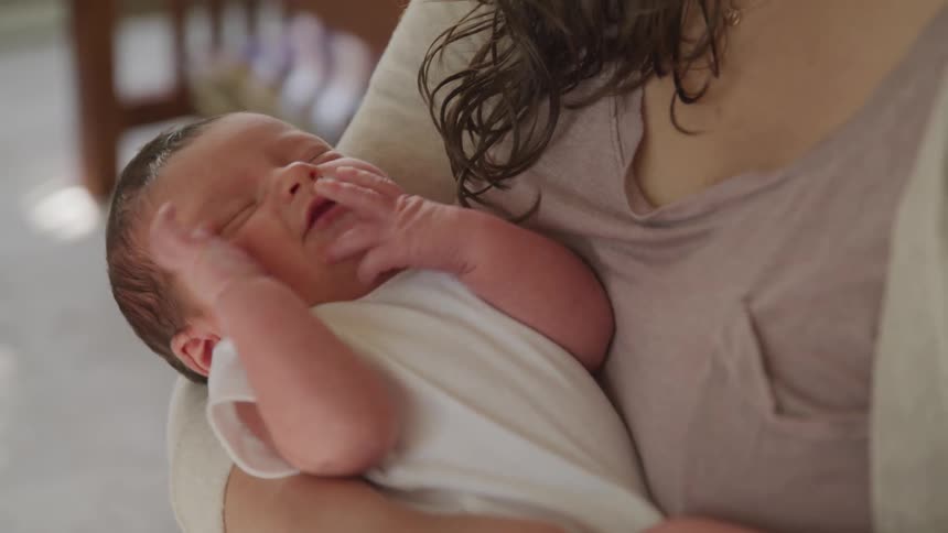 A mother holds her newborn baby who wriggles in her arms before crying