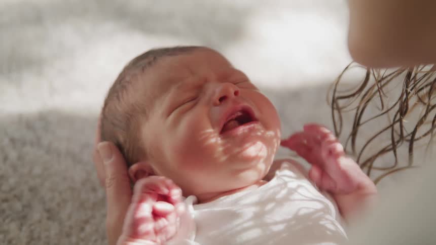 A newborn baby crying and shaking their arms as their mother consoles the child