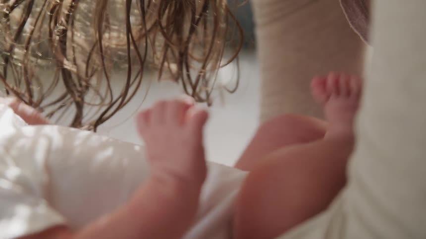 Baby in a white onesie lies on its back and place with its mother