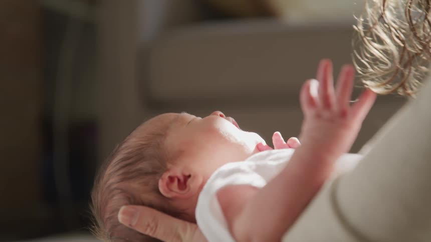 A very small baby squirms and flails its arms while being held by a woman who is trying to sooth it by gently bouncing the baby and rubbing its belly