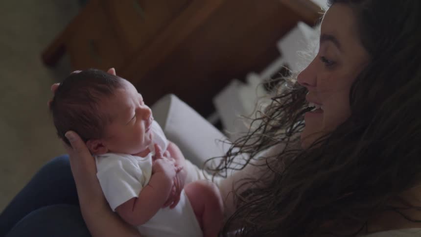 A young mother is holding a newborn baby and kisses their forehead