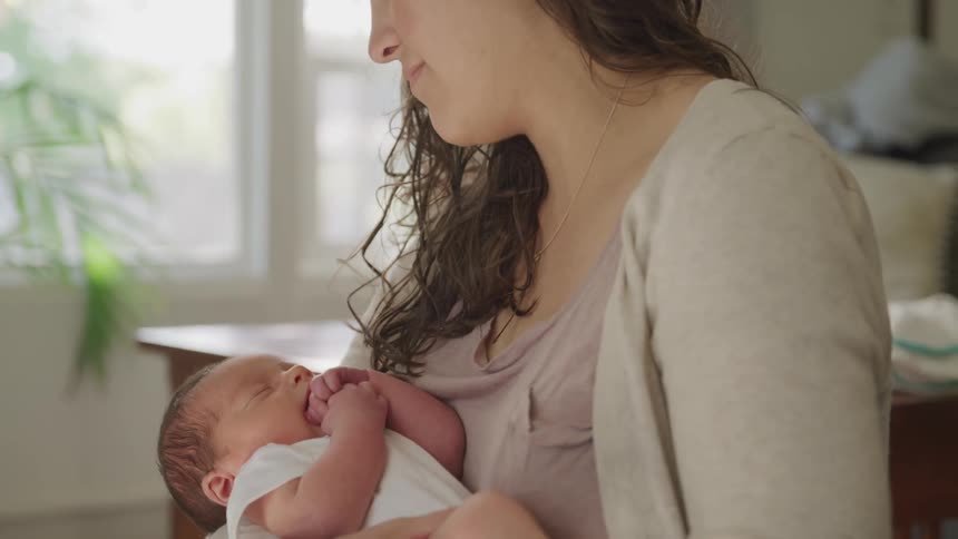 A woman holding a baby while standing around in a house