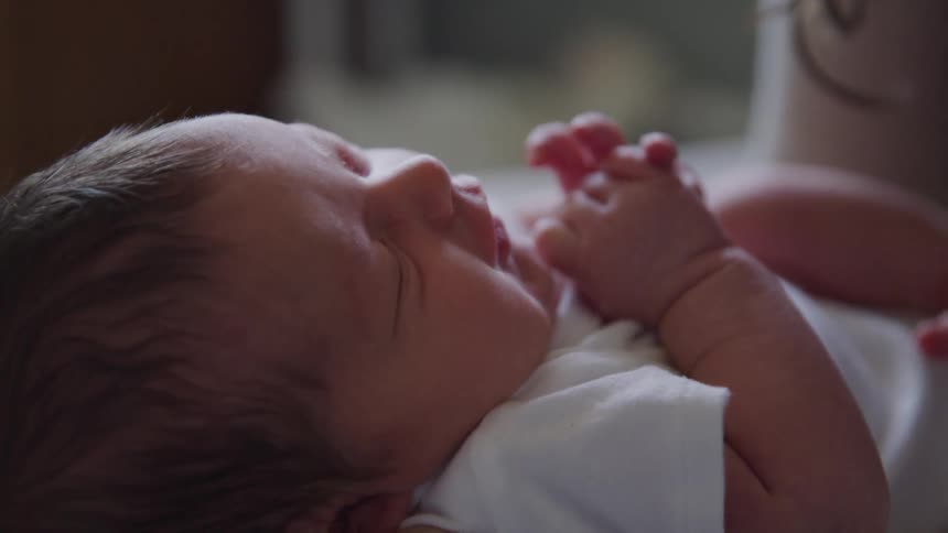 A newborn baby wriggles on the floor as their mother kneels over them
