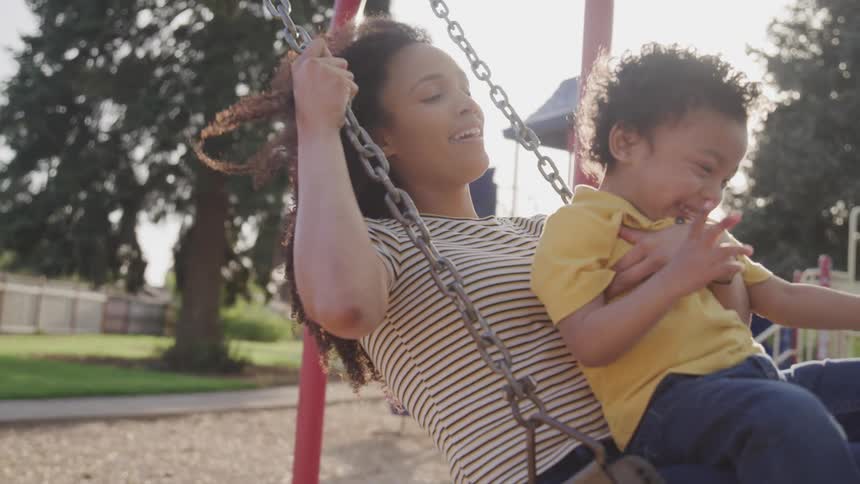 Woman holding child swings in the public park on a sunny day