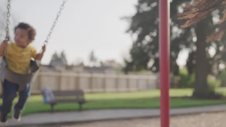 Toddler with yellow shirt play swing at the playground with his mom