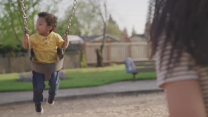 A woman pushes a small boy in a park swing