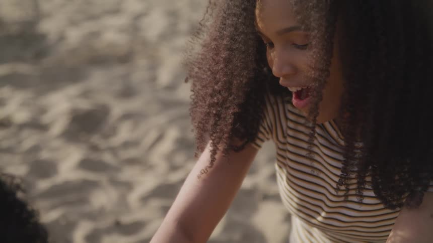 A young woman is smiling and looking surprised as she plays atop some sand with another female
