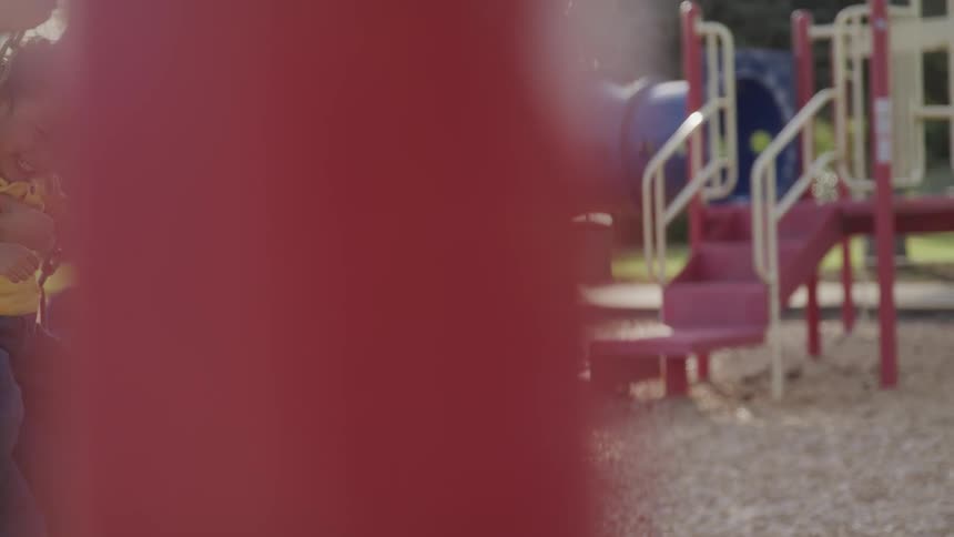 A woman swings on a swing set in the playground while holding a little boy on her lap