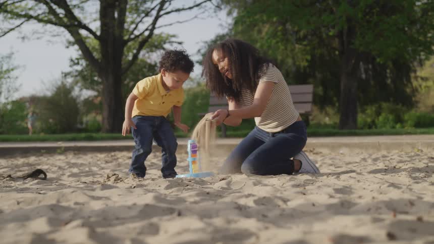 A mother and son play in a sand box at a park on a summer day