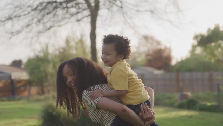 Brunette woman gives the boy a piggyback ride on green field during daylight