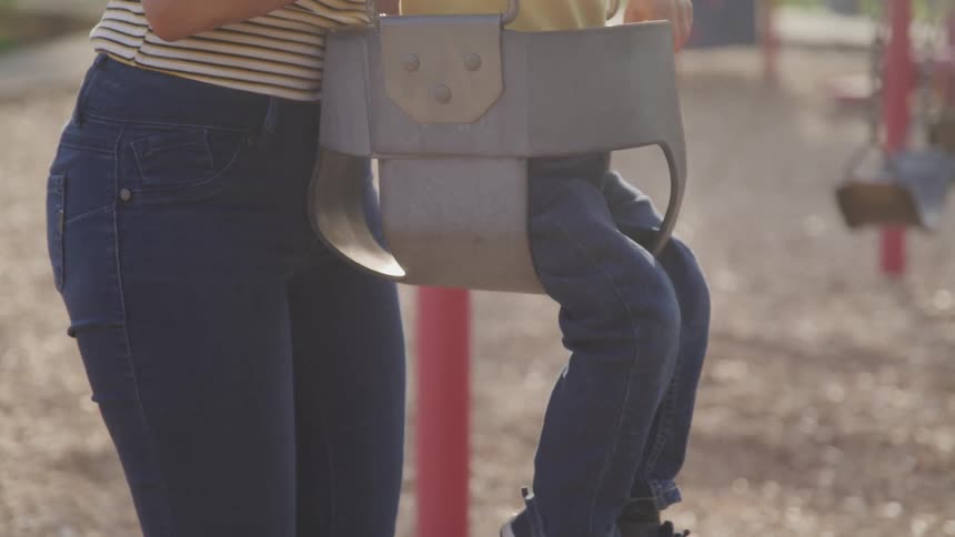 A woman puts a small child in a swing at the park