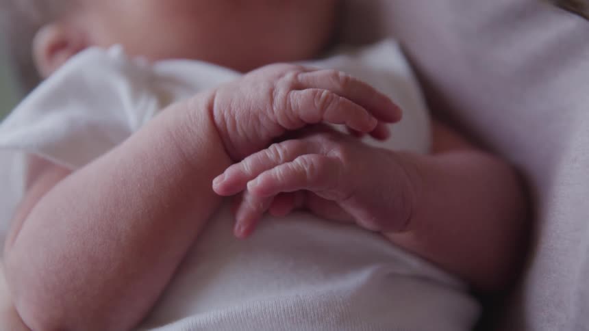 A baby lays on a blanket moving its hands