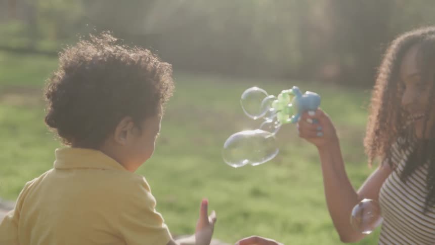 A woman sprays bubbles playing with her child on the grass