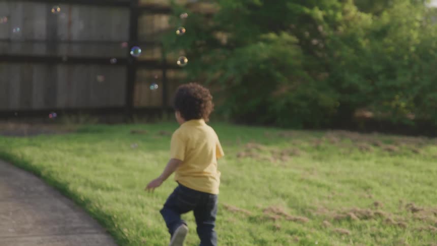 A boy chases bubbles in a yard on a sunny day