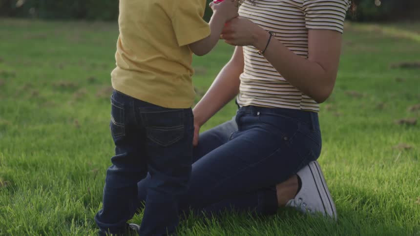 A mother and young son play outside on a grassy lawn