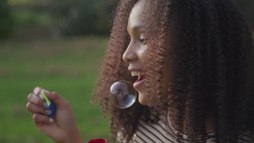 A young black woman blowing bubbles in a field