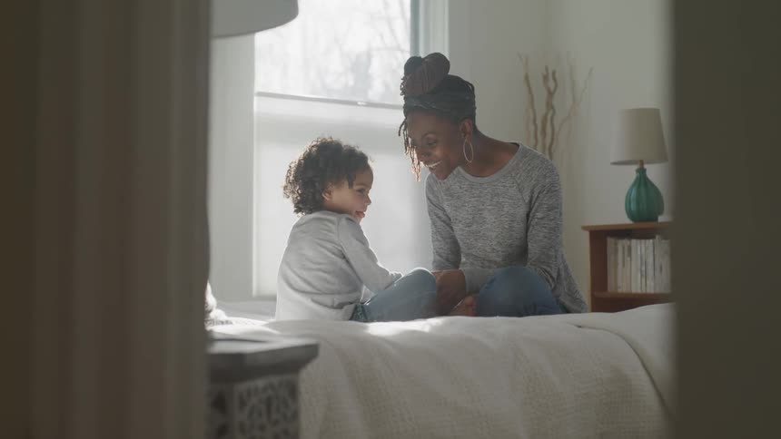 A mother and child smile and hold hands while sitting in bed