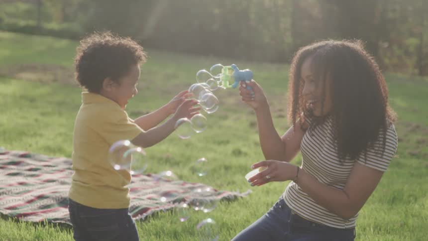 A woman uses a toy bubble machine to play with a small child