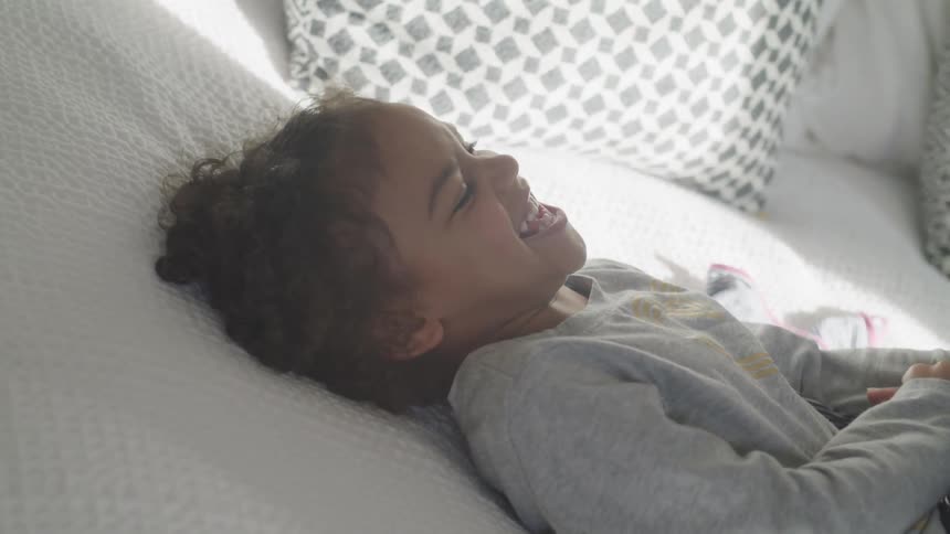 A little girl being tickled while laying on a bed