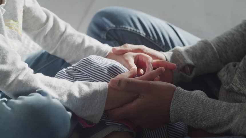 Woman and child sit cross legged and hold each others hand indoors during daylight