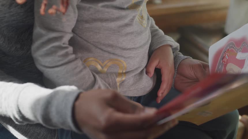 Parent reads picture book to child sitting in their lap