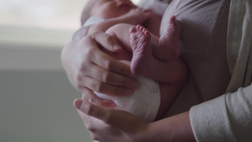 A woman cradling a baby near a window