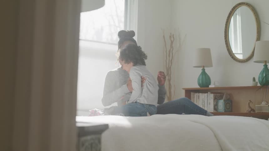 Mother cuddles child on her lap while sitting on bed