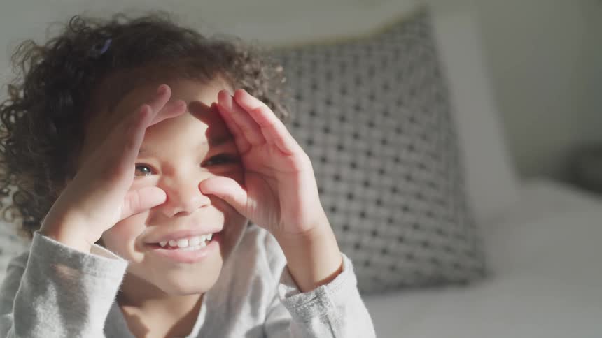 A young girl has her hands up to her face and smiling as she is listening to and playing a game with an adult woman