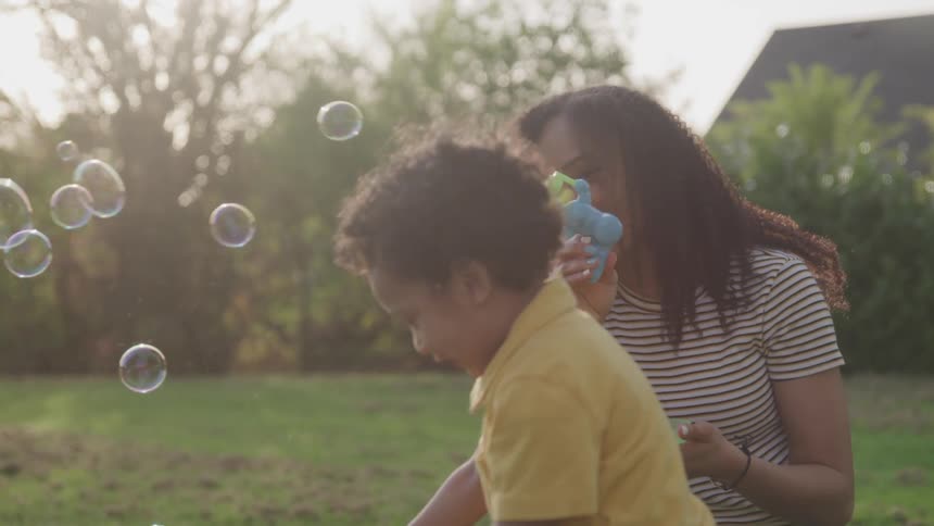 A woman blows bubbles for her son to play with in the yard