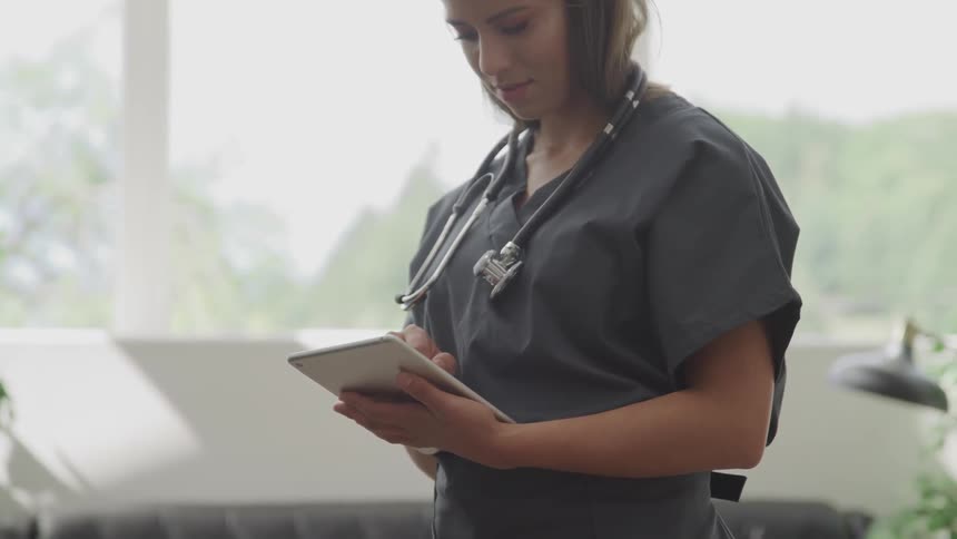 A woman with scrubs and a stethoscope touching a tablet