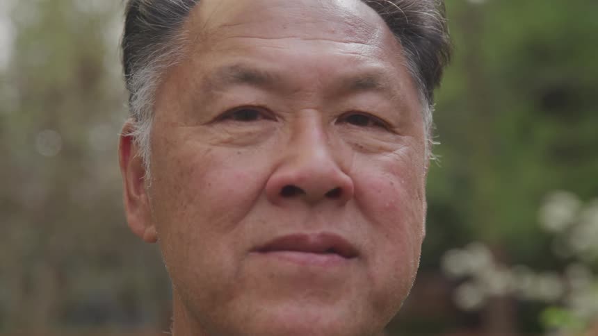 An asian man standing outdoors turning to look at the camera
