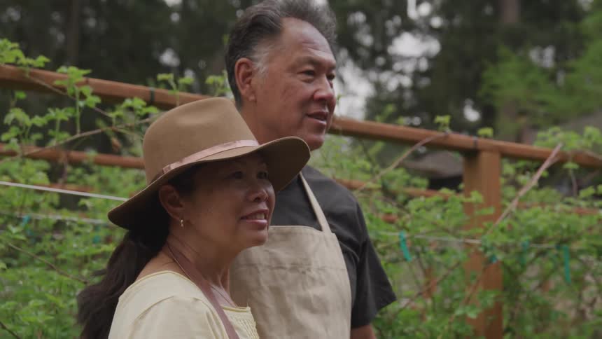 An older couple wearing aprons standing together outdoors during the day