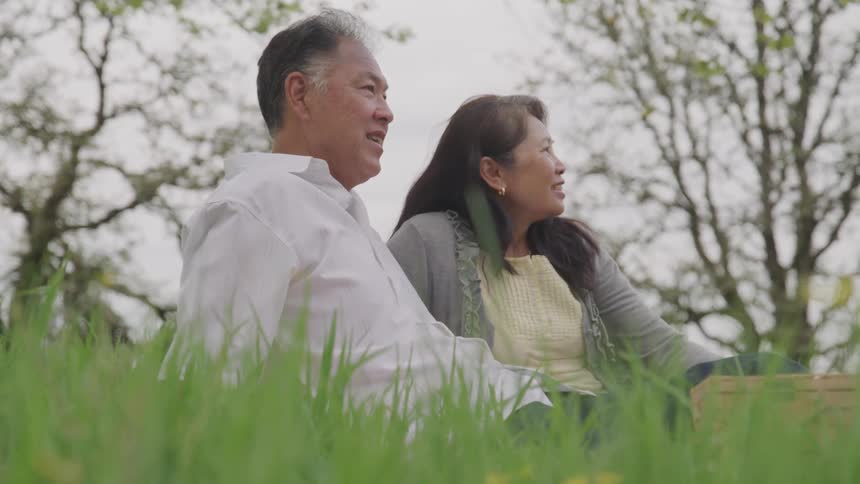 Asian man and woman sit on the green grass in the forest during daylight