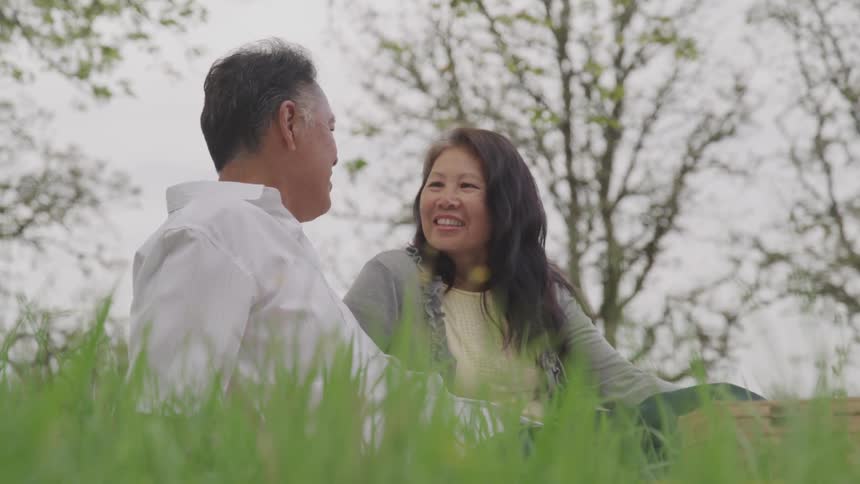 A husband and wife smile and chat while sitting in the grass