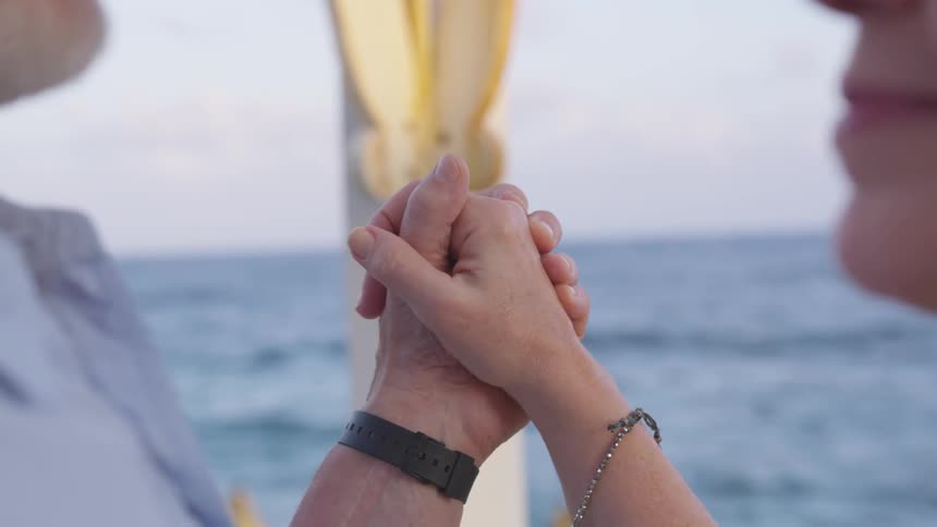 Man and woman hold hands and look at each other while dancing next to the seaside during daylight