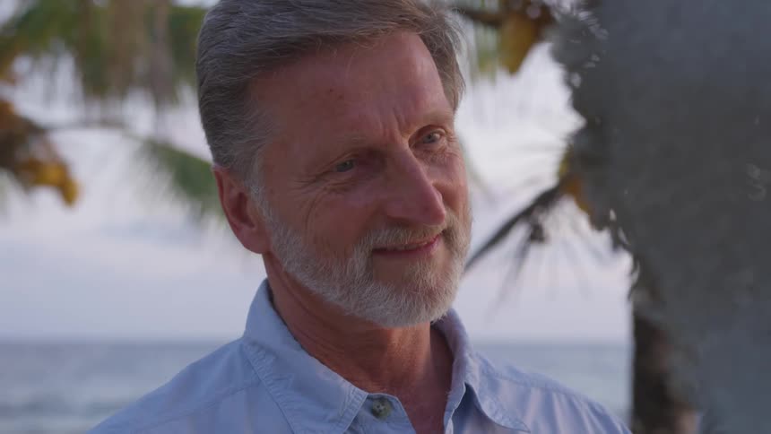 Man smiles as he stands near a palm tree