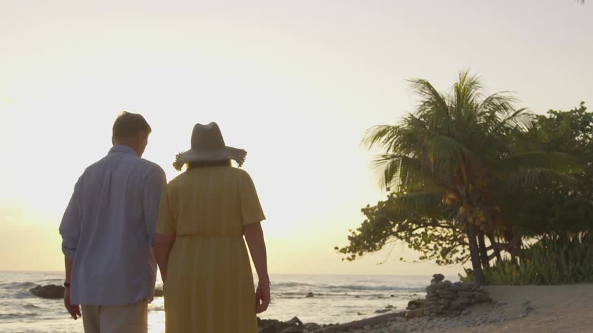 A caucasian male female couple walking on a beach near trees