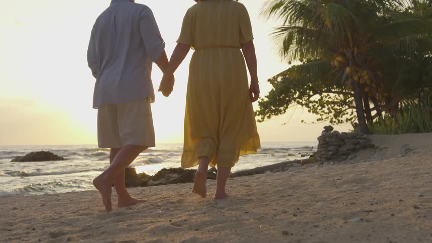 Couple walking on a beach holding hands at sunset