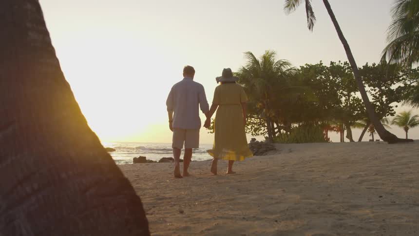 A man and woman walk on the beach holding hands