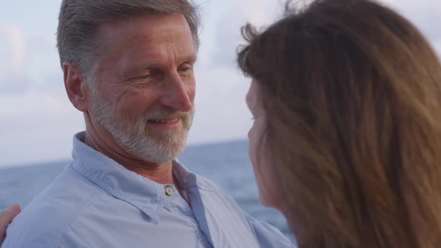 Man and woman embrace as they stand near the ocean