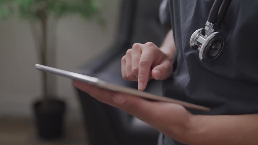 A medical professional with a stethoscope around their neck uses a tablet